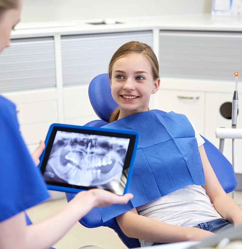 Child in dental chair with dentist holding x-rays display on tablet